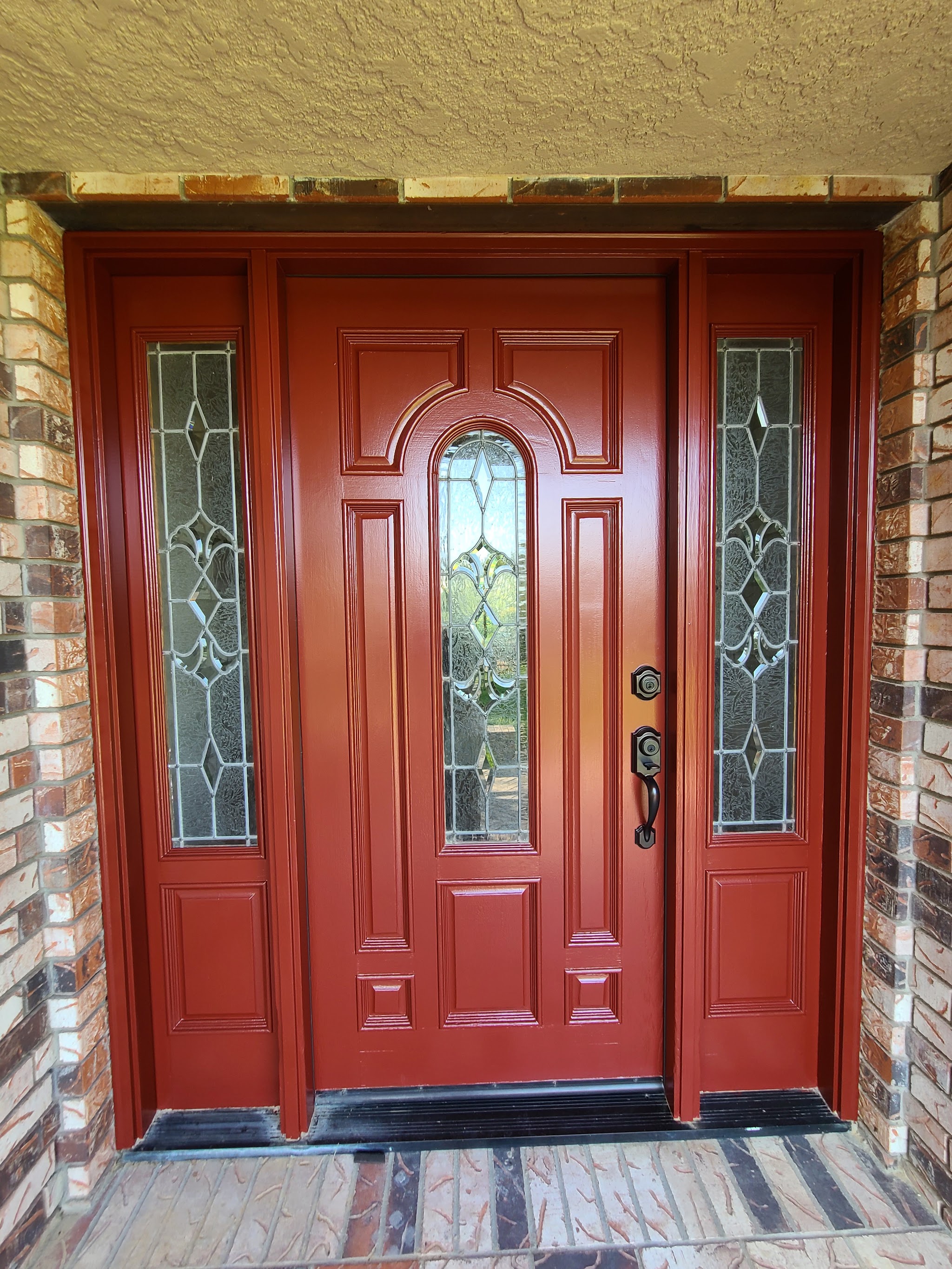 Freshly repainted red front door with glass sidelights on a brick exterior